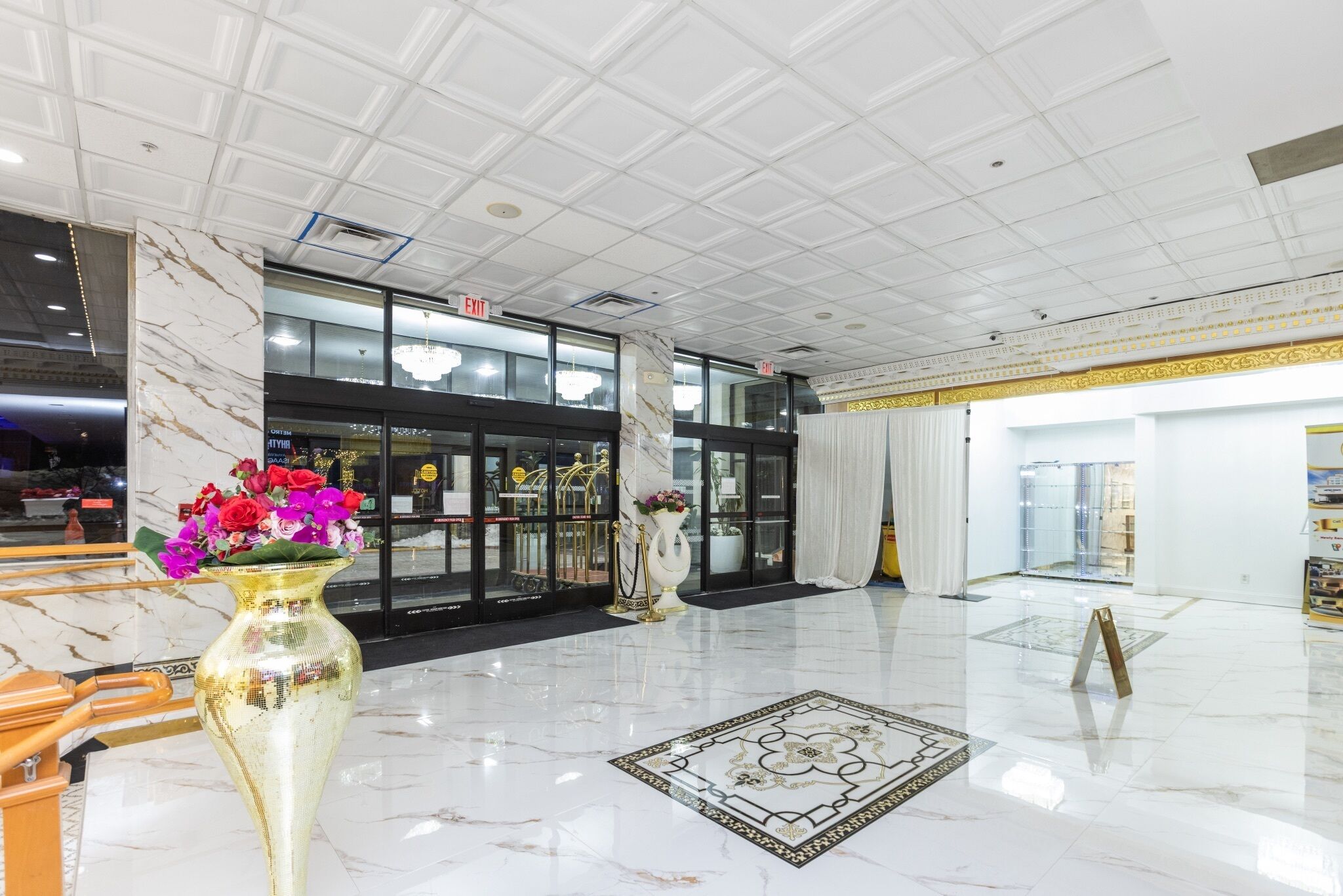 En hotellobby med marmorgolv, en stor vas med blommor och en kristallkrona.