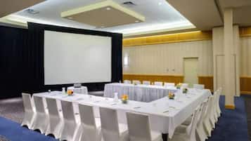 Un salón de conferencias con una larga mesa, sillas blancas y una pantalla de proyector.