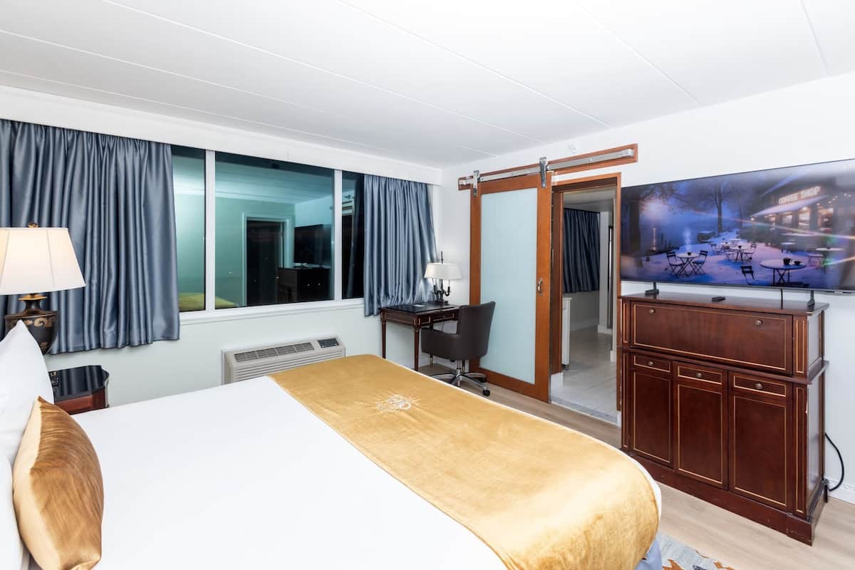 Une chambre d’hôtel équipée d’un lit, d’un bureau, d’une chaise, d’une télévision et d’une grande fenêtre avec des rideaux.