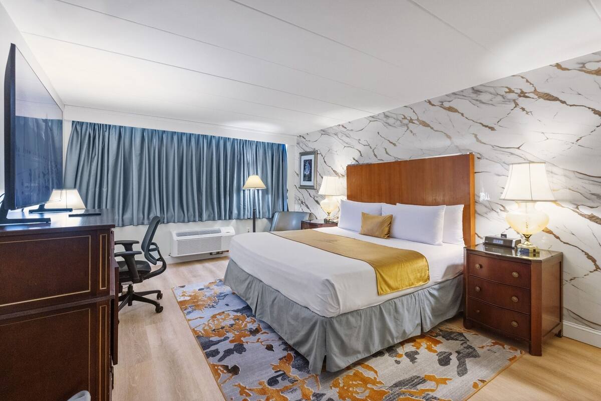 Une chambre d’hôtel équipée d’un lit, d’un bureau, d’une chaise, de lampes et d’un mur décoré d’un motif imitant le marbre.
