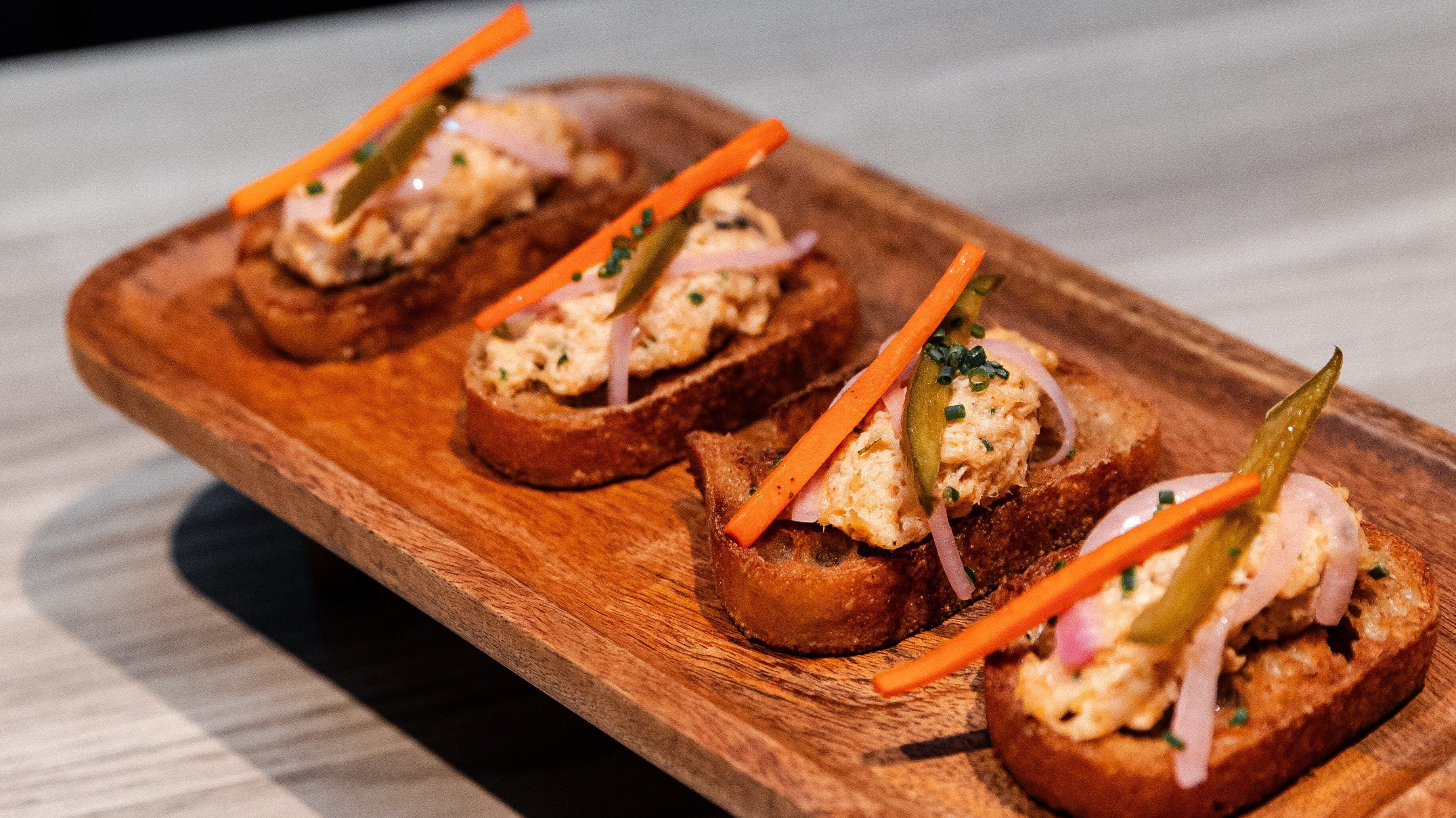 Tres sándwiches abiertos sobre una tabla de madera.