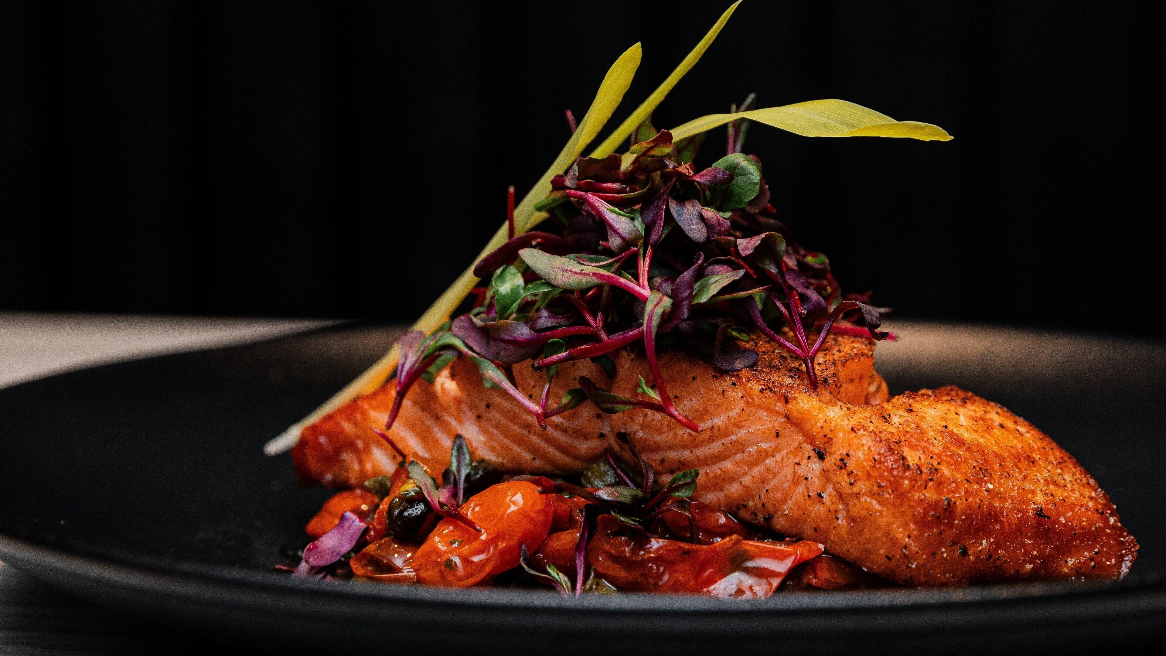 A plate of cooked salmon with a garnish of greens and cherry tomatoes.