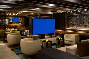 Et moderne hotelværelse med stort fladskærms-tv, komfortable siddepladser, et barområde og en dekorativ væg af tallerkener.