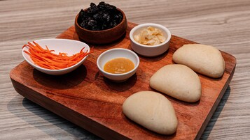 A wooden board with various food items including dumplings, shredded carrots, and two small bowls of sauce.