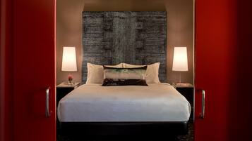 A hotel room with a large bed, two bedside lamps, a decorative headboard, and a red door.