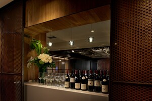 Zona de bar con botellas de vino, copas, paneles de madera y un arreglo floral decorativo.