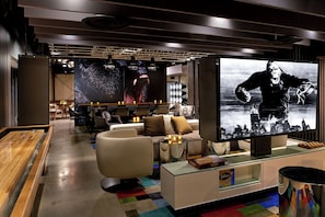 A modern lounge area with a foosball table, comfortable seating, a large flat-screen TV, and a Scrabble set on a glass table.