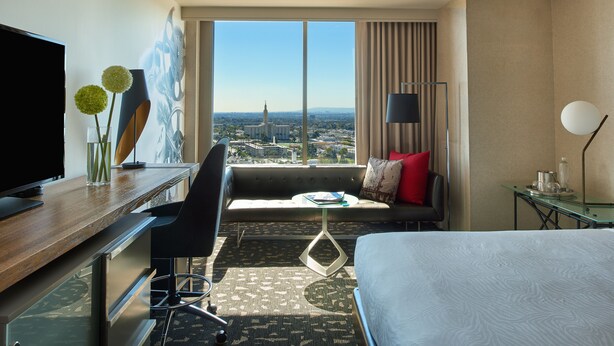 Ein Hotelzimmer mit einem Bett, einem Schreibtisch mit Fernseher, einem Sessel, einer Couch, einem kleinen Tisch und Blick auf die Stadt.