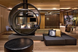 A modern lounge area with a circular fire feature, seating, and a television.