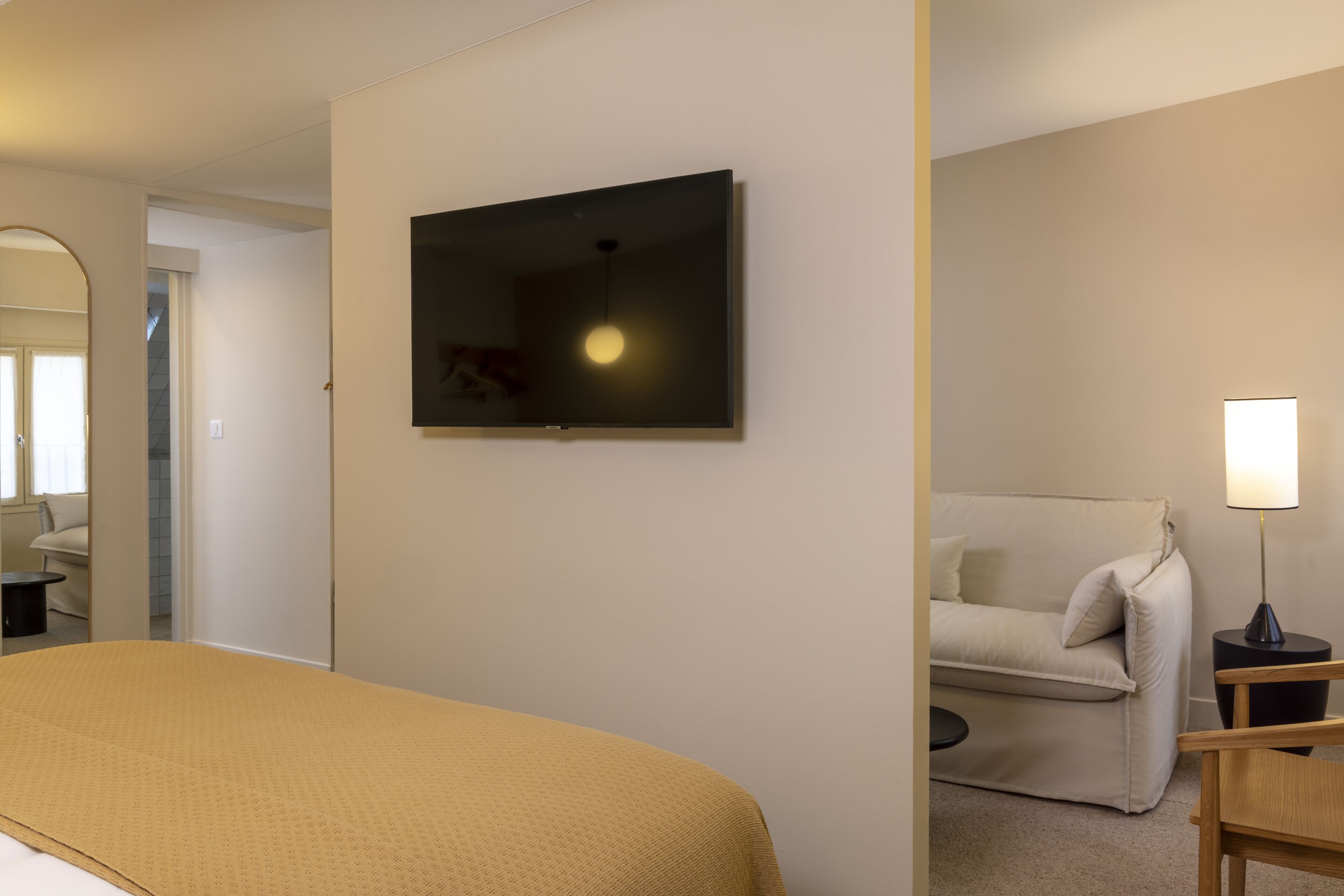 A hotel room with a bed, a television mounted on the wall, a sofa, and a lamp.