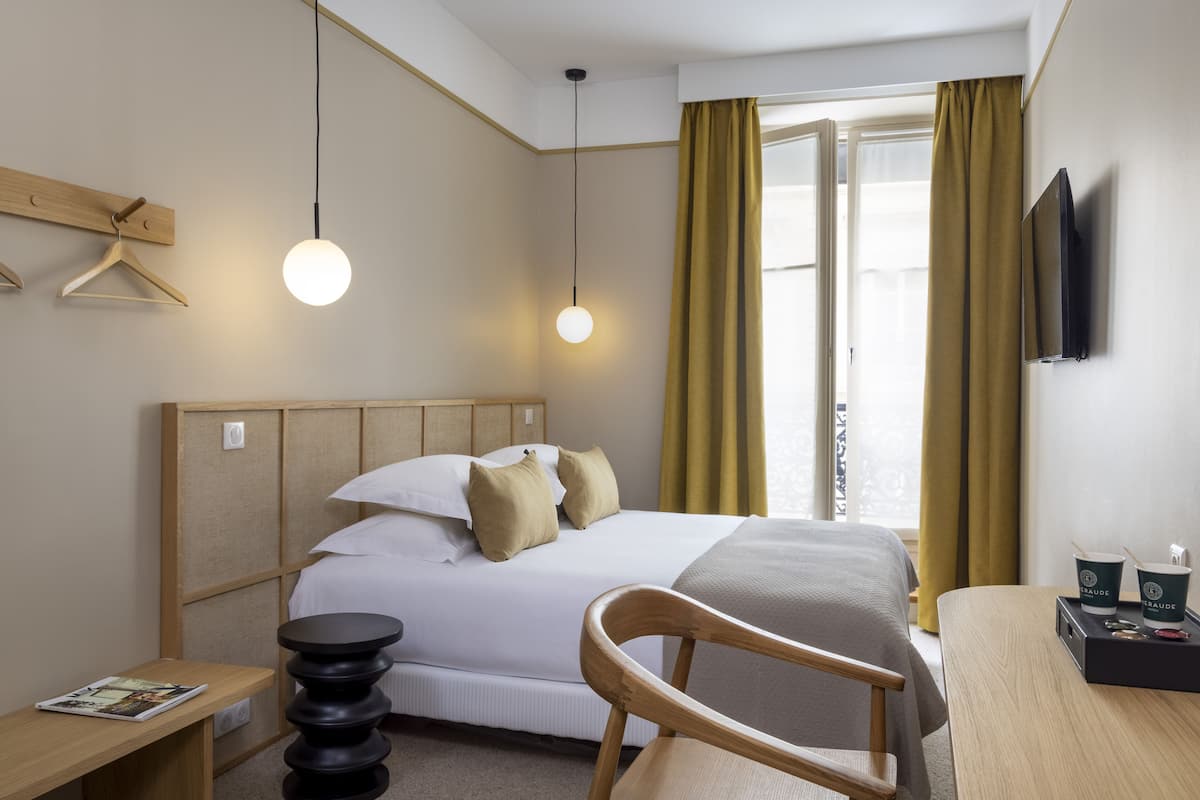 A hotel room with a bed, wooden headboard, bedside table, chair, and a TV mounted on the wall.