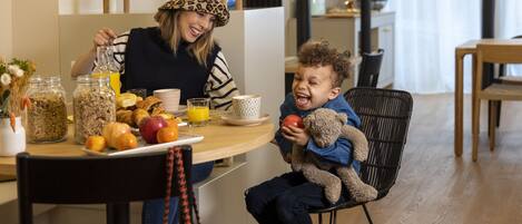 Un coin repas avec une table mise pour le petit-déjeuner, comprenant des fruits, un ours en peluche et un verre de jus d’orange.