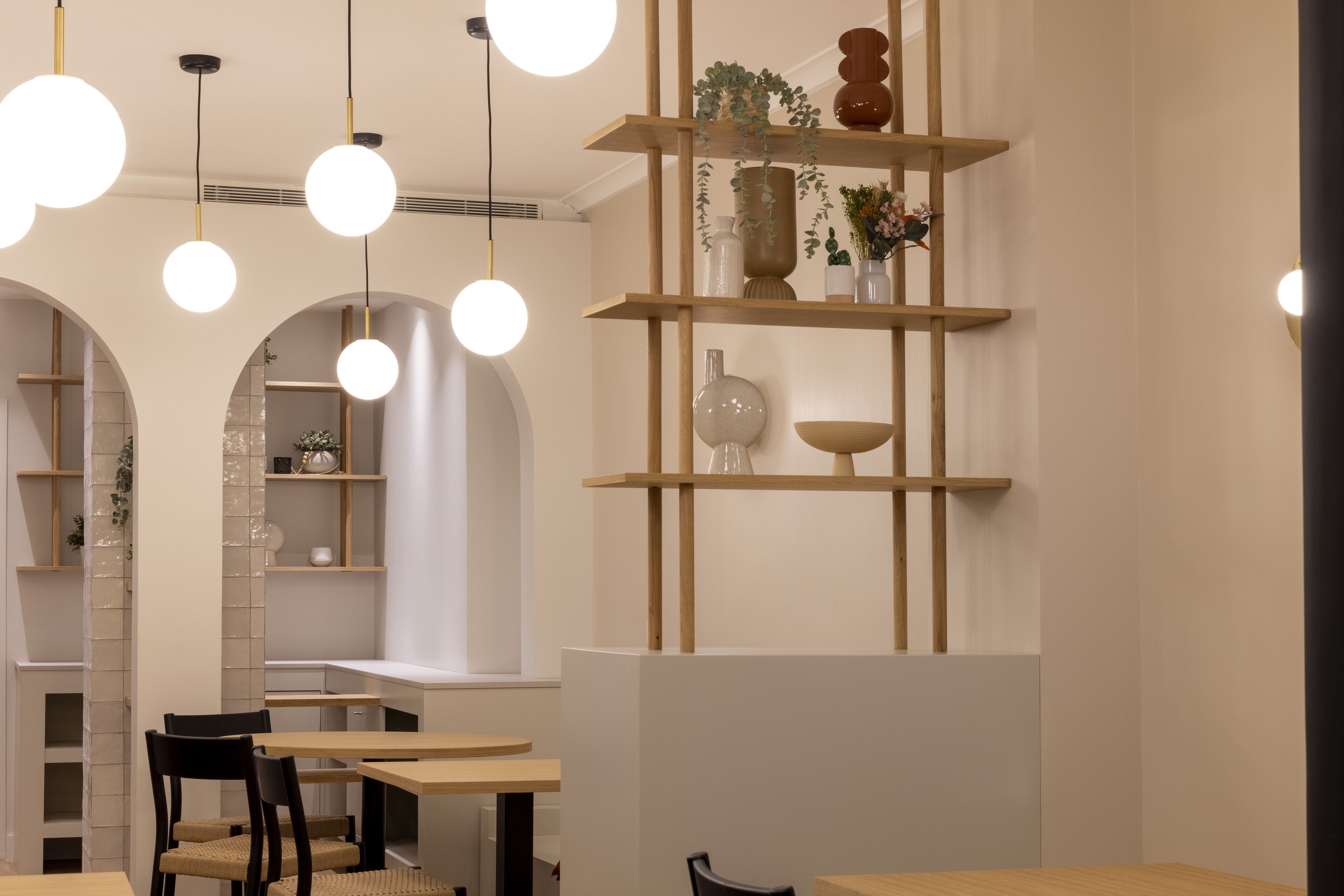 Un interior moderno con estanterías de madera, lámparas colgantes redondas y una zona de estar con mesas y sillas.