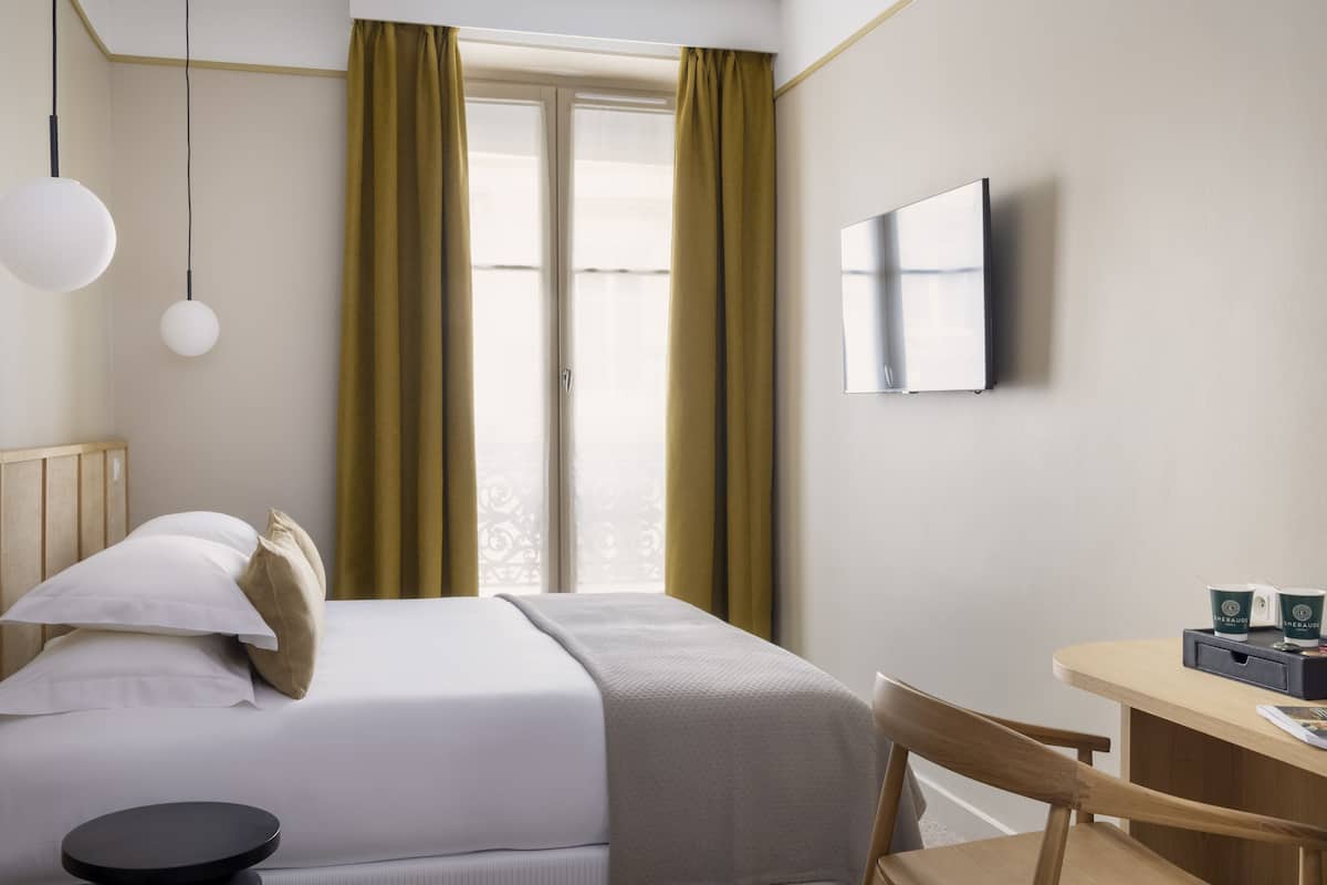 A hotel room with a bed, a desk, a chair, a TV, and a window with curtains.