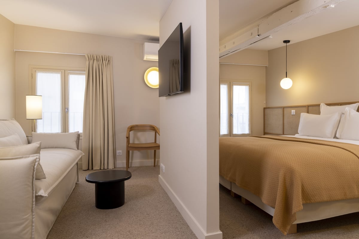 A hotel room with a bed, a sofa, a chair, a TV, and a lamp.