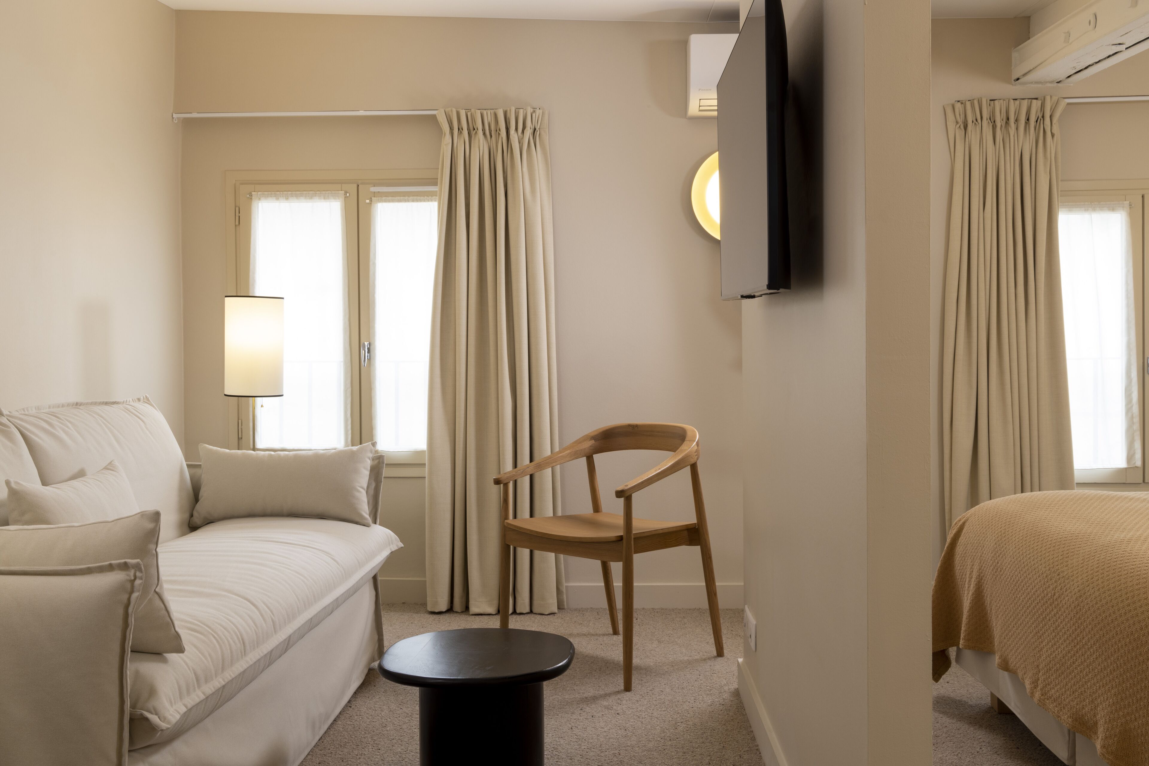 A hotel room with a bed, a sofa, a chair, a TV, and curtains.