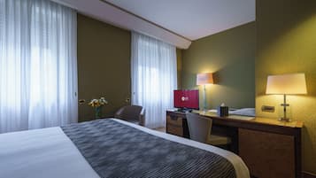 Ein Hotelzimmer mit einem großen Bett, einem Schreibtisch, einem Stuhl, einem Fernseher und einer Lampe.