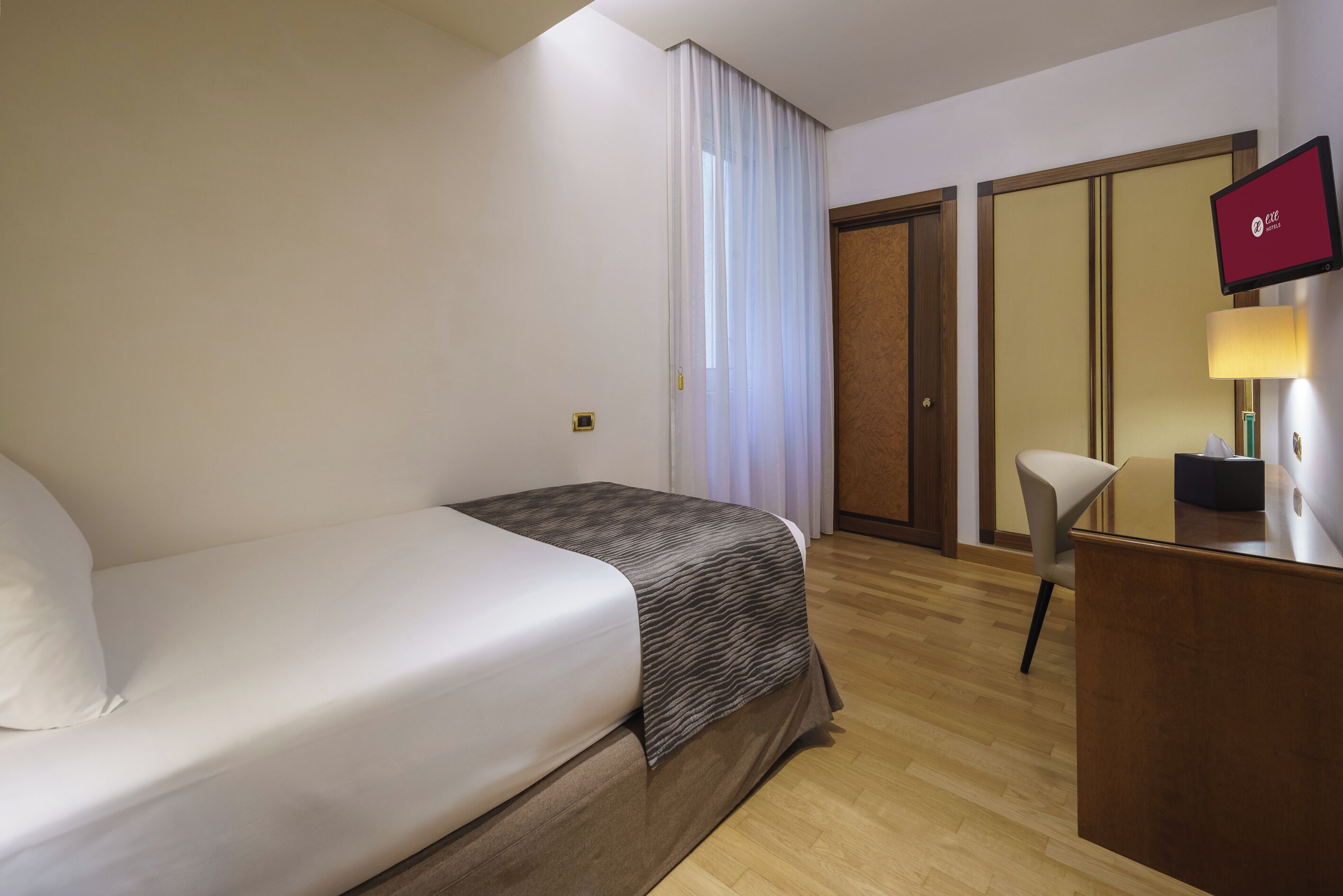 Une chambre d’hôtel équipée d’un lit, d’un bureau, d’une chaise, d’une télévision et d’une armoire.