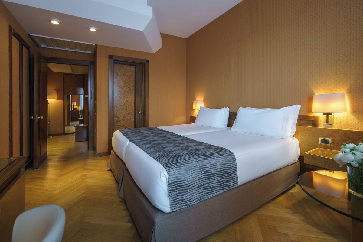 Une chambre d’hôtel avec un grand lit, des lampes de chevet, une table en verre et une chaise.