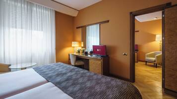 Une chambre d’hôtel avec un grand lit, un bureau avec un ordinateur portable, une chaise, une table ronde et une porte donnant sur une autre pièce.