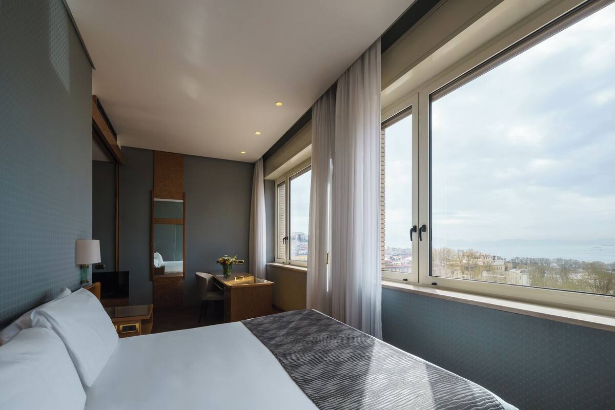 Une chambre d’hôtel avec un grand lit, un bureau, une chaise, une télévision et une fenêtre donnant sur la ville.