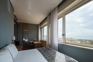 Habitación de hotel con una cama grande, un escritorio, una silla, un televisor y una ventana con vista a la ciudad.