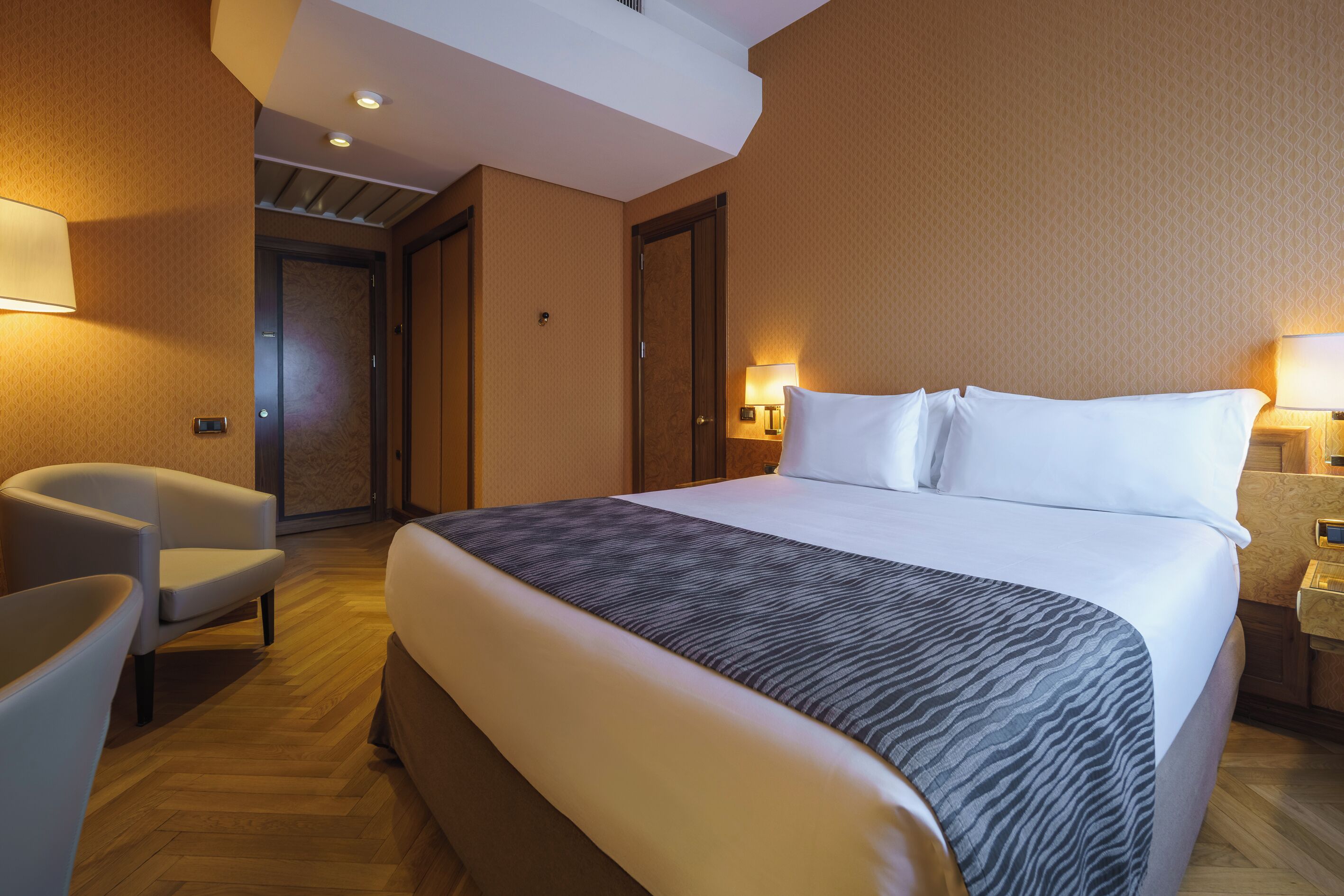 Une chambre d’hôtel avec un grand lit, une chaise, un bureau et une porte donnant sur une autre pièce.