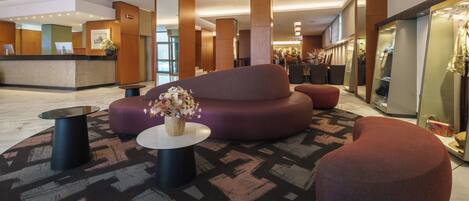 A lobby with a reception desk, a seating area with a sofa and ottoman, and a mirror reflecting the space.