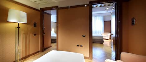 A hotel room with a bed, a chair, a lamp, and a door leading to another room.
