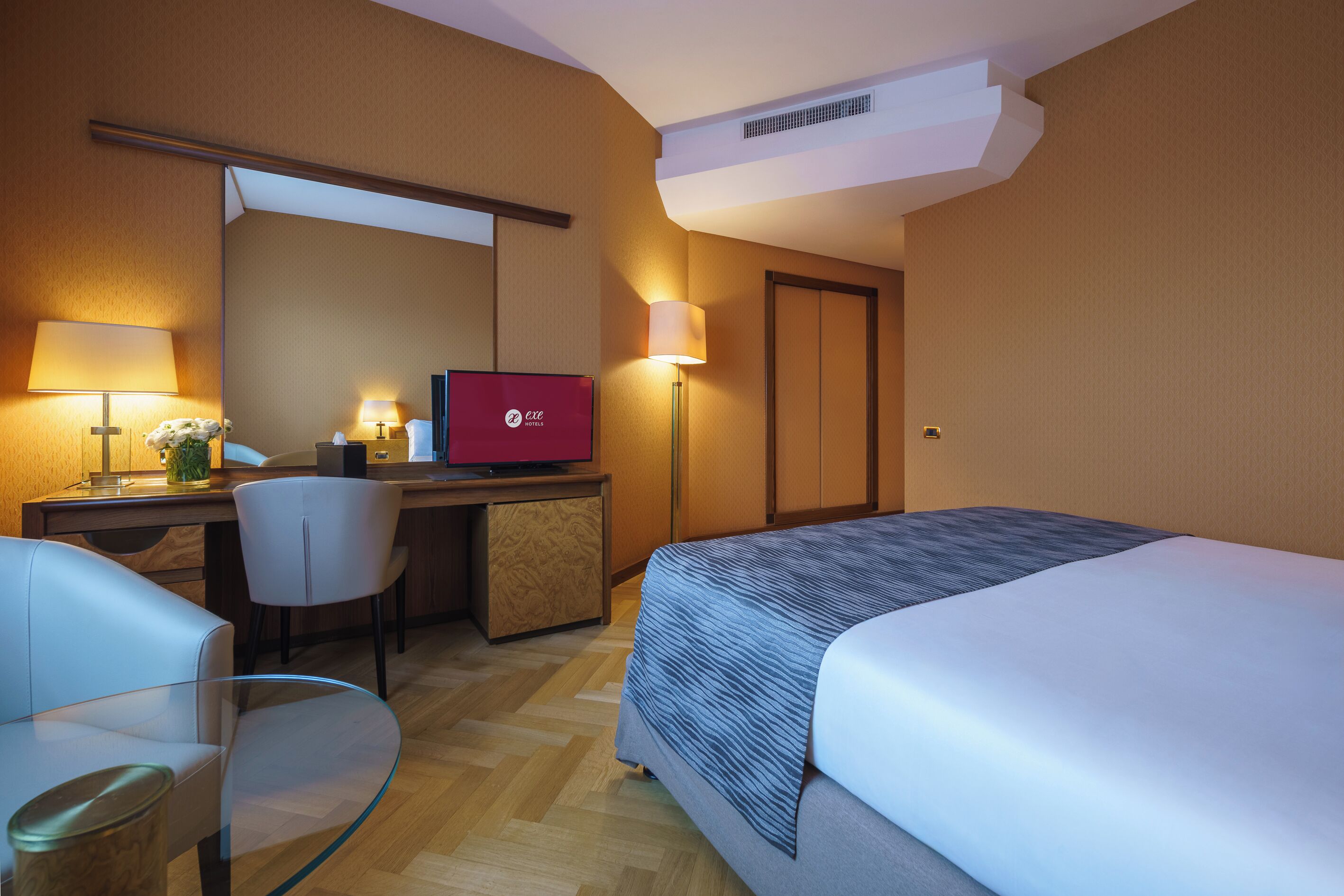 Une chambre d’hôtel avec un lit, un bureau avec un ordinateur, une chaise et une lampe.