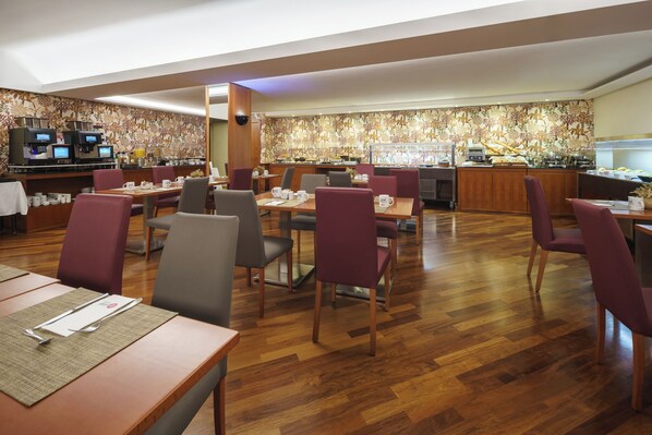 Un comedor de hotel con varias mesas y sillas, una estación de café y un bufé.