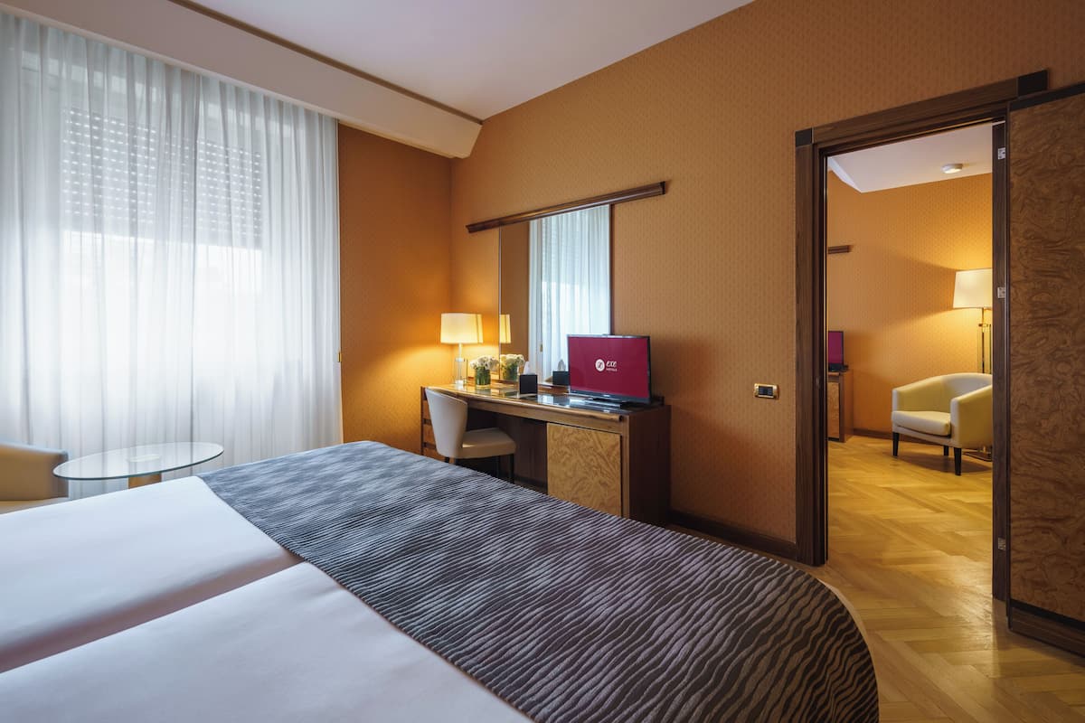 Une chambre d’hôtel avec un grand lit, un bureau avec un ordinateur portable, une chaise, une table ronde et une porte donnant sur une autre pièce.