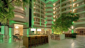 Vestíbulo de hotel de varios niveles con una zona de bar central, múltiples balcones y plantas de interior.