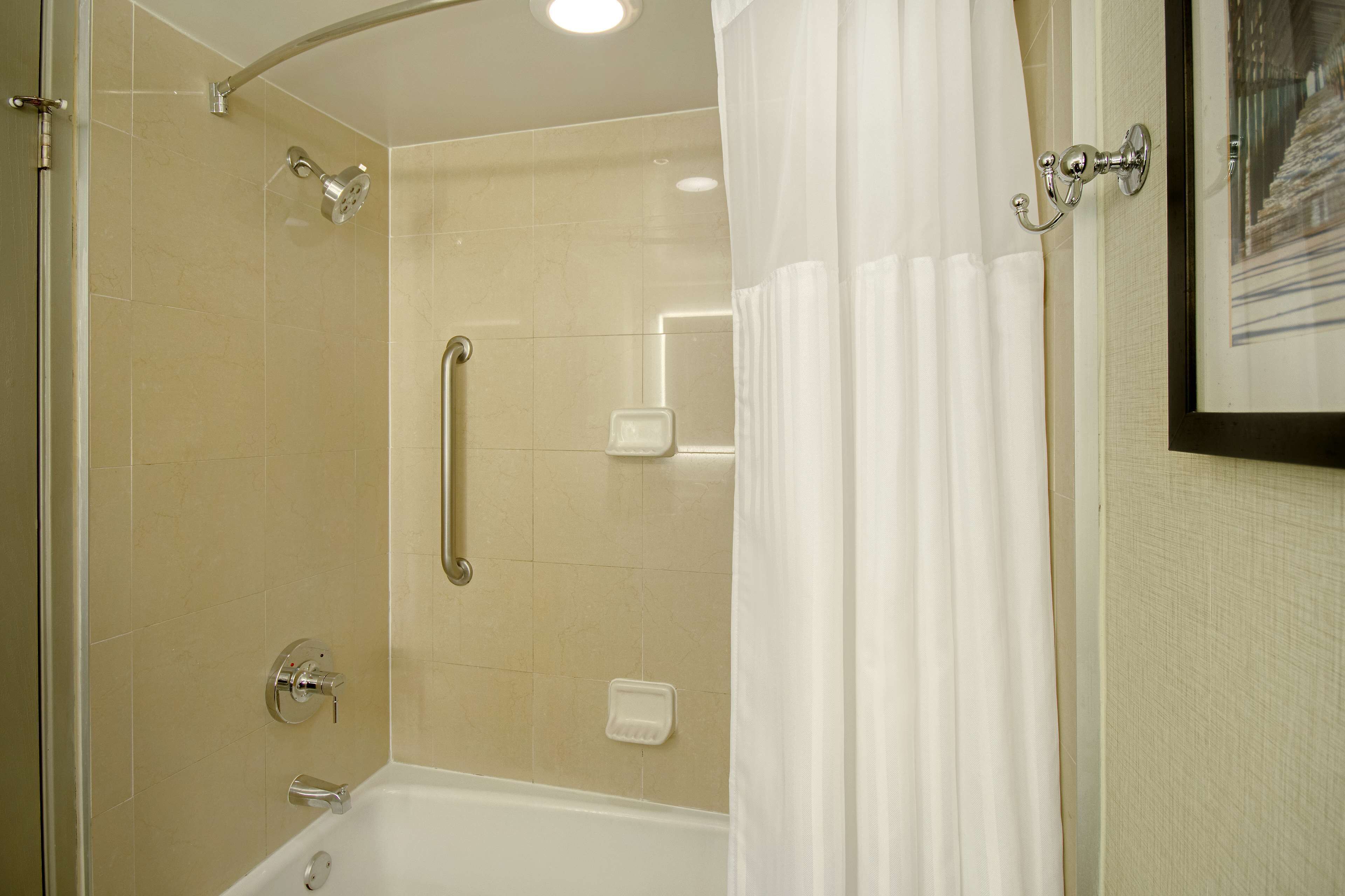 A shower area with a glass door, a handheld showerhead, and a white bathtub.