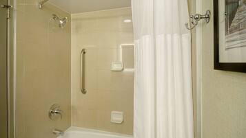 A shower area with a glass door, a handheld showerhead, and a white bathtub.
