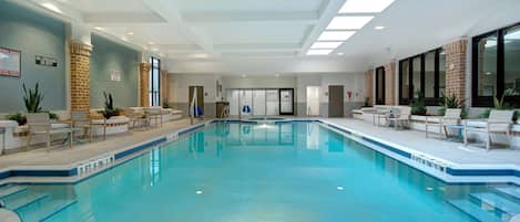 Una piscina interior con agua cristalina, rodeada de sillones de descanso y plantas en macetas.
