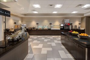 A hotel buffet area with labeled food stations, a Coca-Cola refrigerator, and a variety of fruits on the counter. - Embassy Suites by Hilton Jacksonville Baymeadows (Jacksonville)