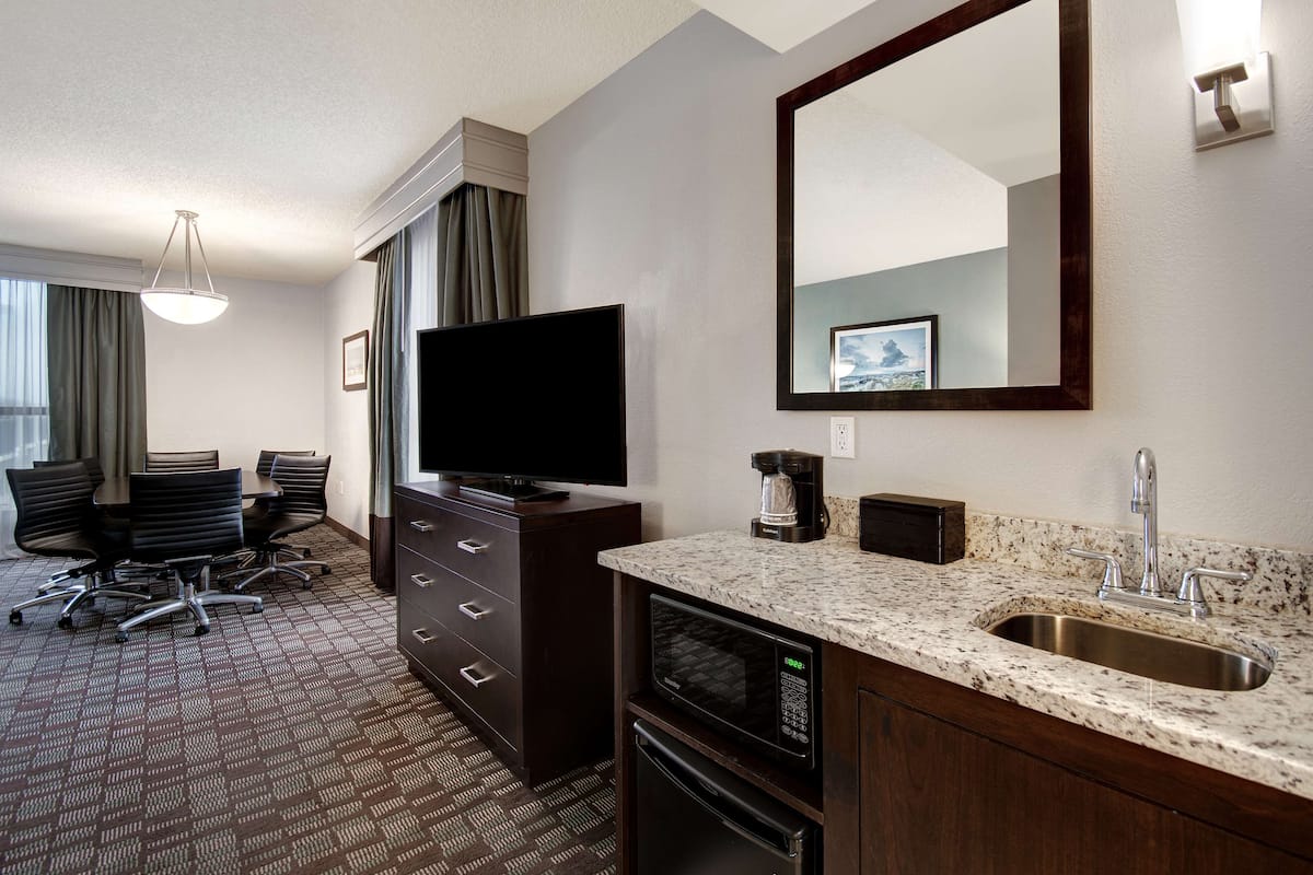 Habitación de hotel con televisión de pantalla plana, cafetera, microondas, lavamanos y una mesa de conferencias con sillas.