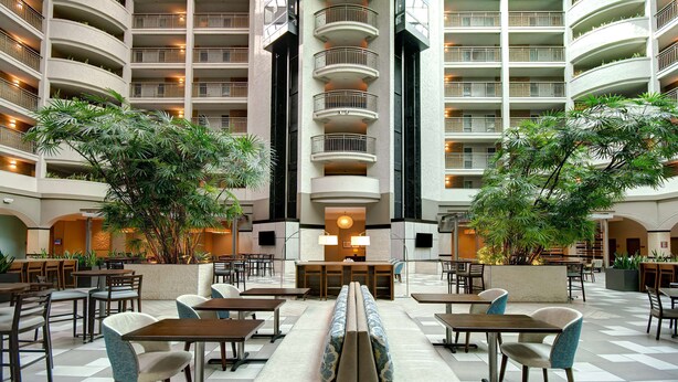 Un amplio vestíbulo de hotel con varios pisos, una escalera central y abundante vegetación de interior.