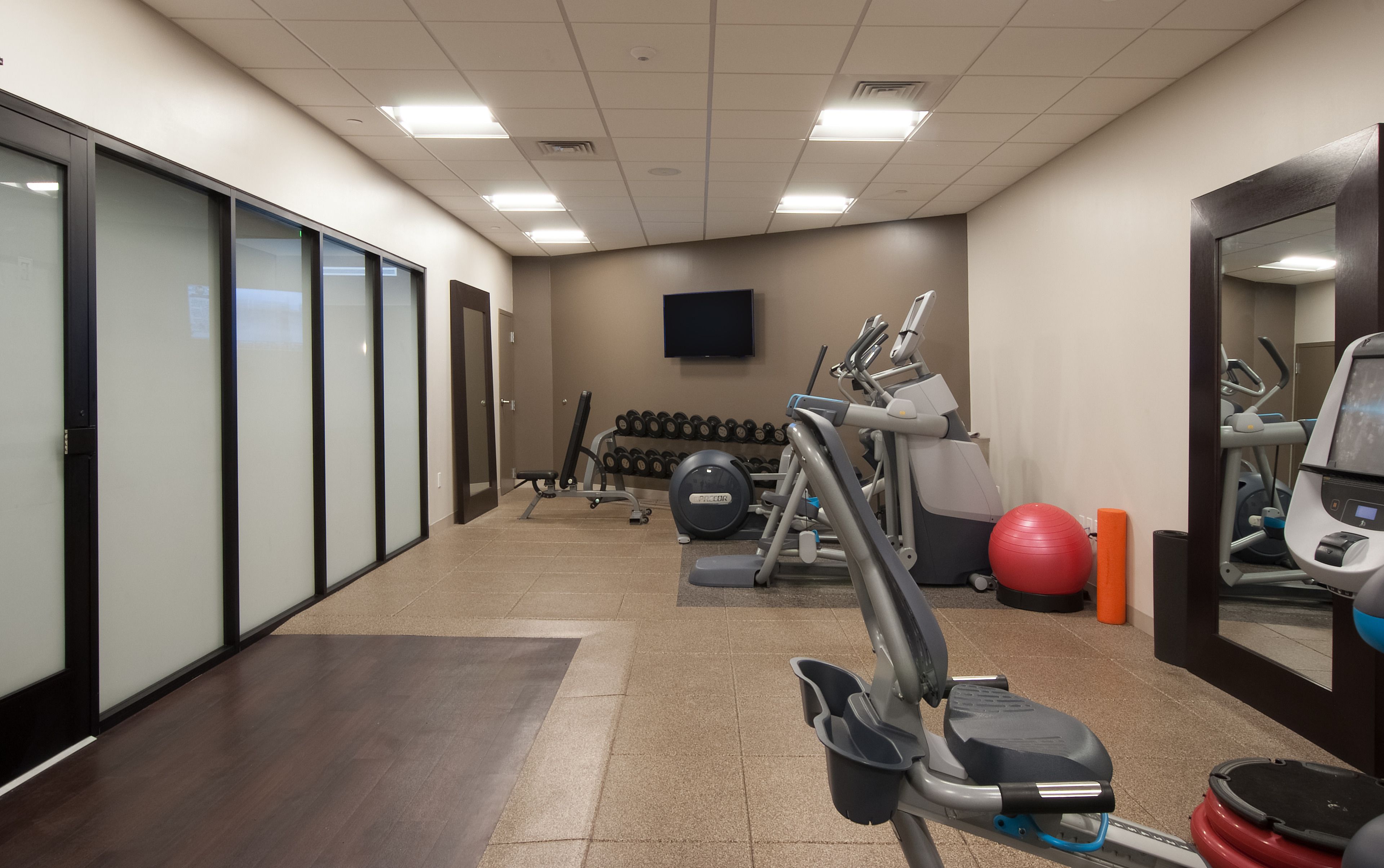 Un gimnasio con equipo de ejercicio, una televisión y un espejo.