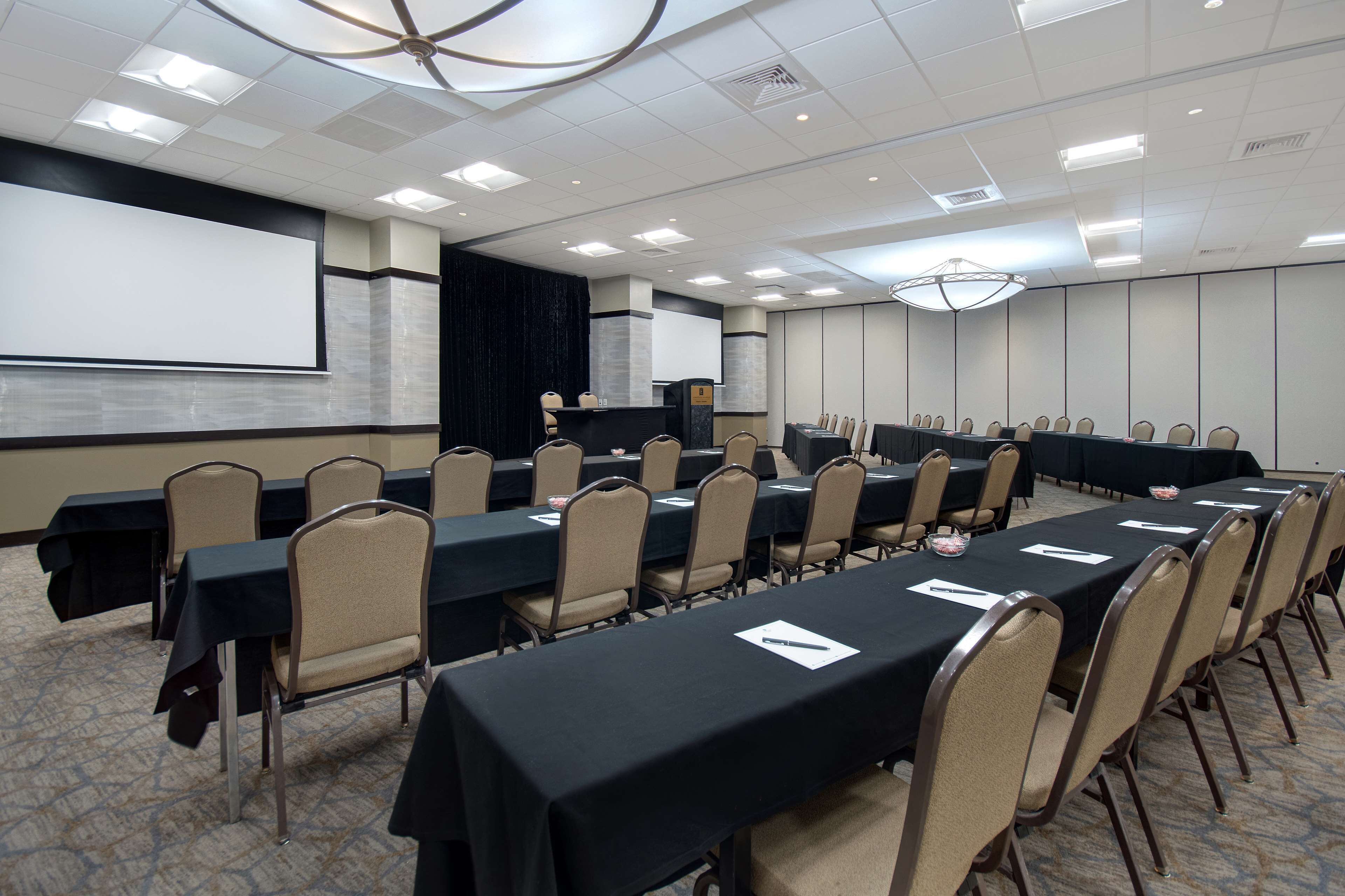 A conference room with long tables, chairs, a projector screen, and a presentation podium.