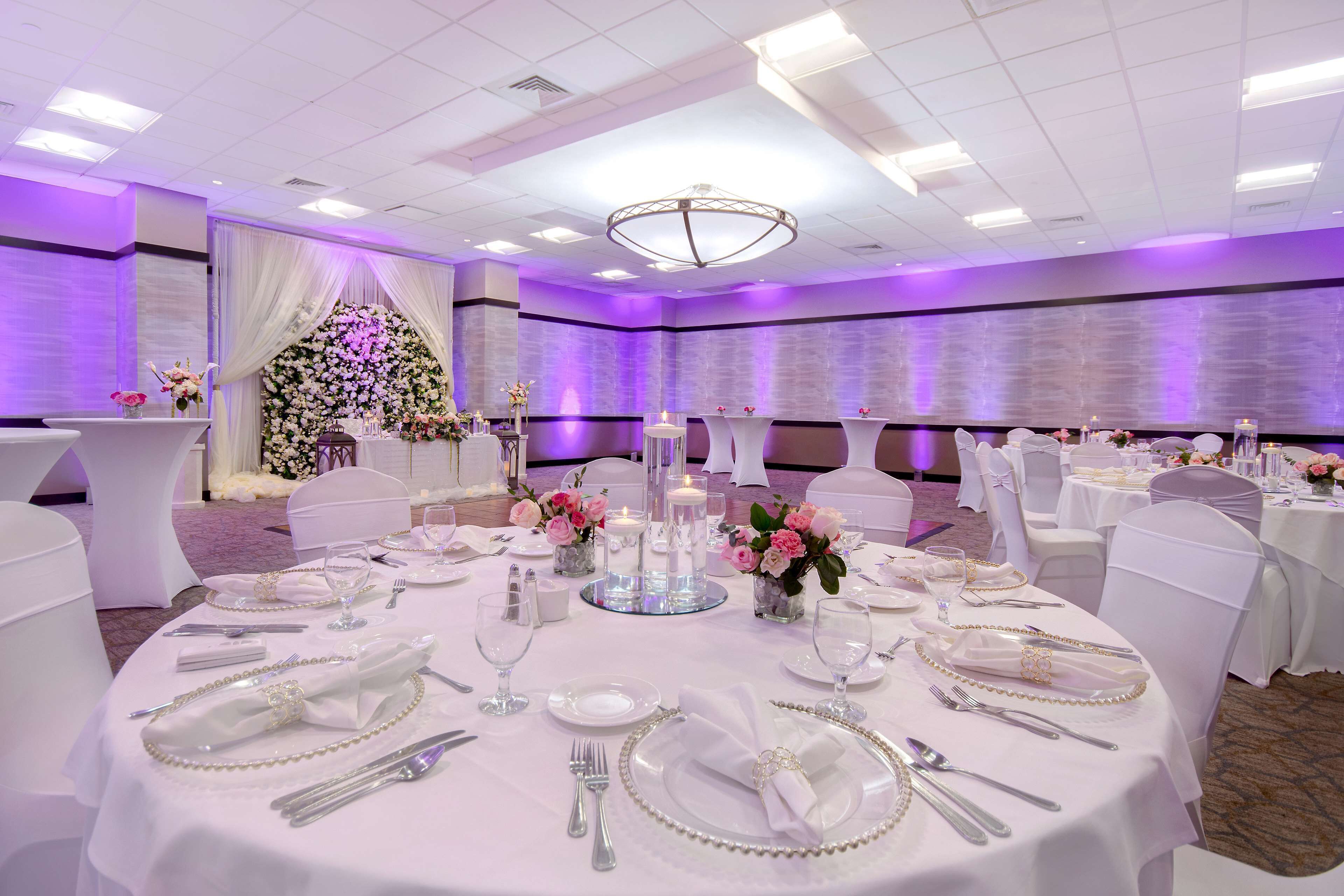 Un salón de banquetes con mesas redondas dispuestas para un evento formal, con manteles blancos, cubertería y centros de mesa florales.
