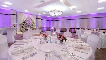 Un salón de banquetes con mesas redondas dispuestas para un evento formal, con manteles blancos, cubertería y centros de mesa florales.