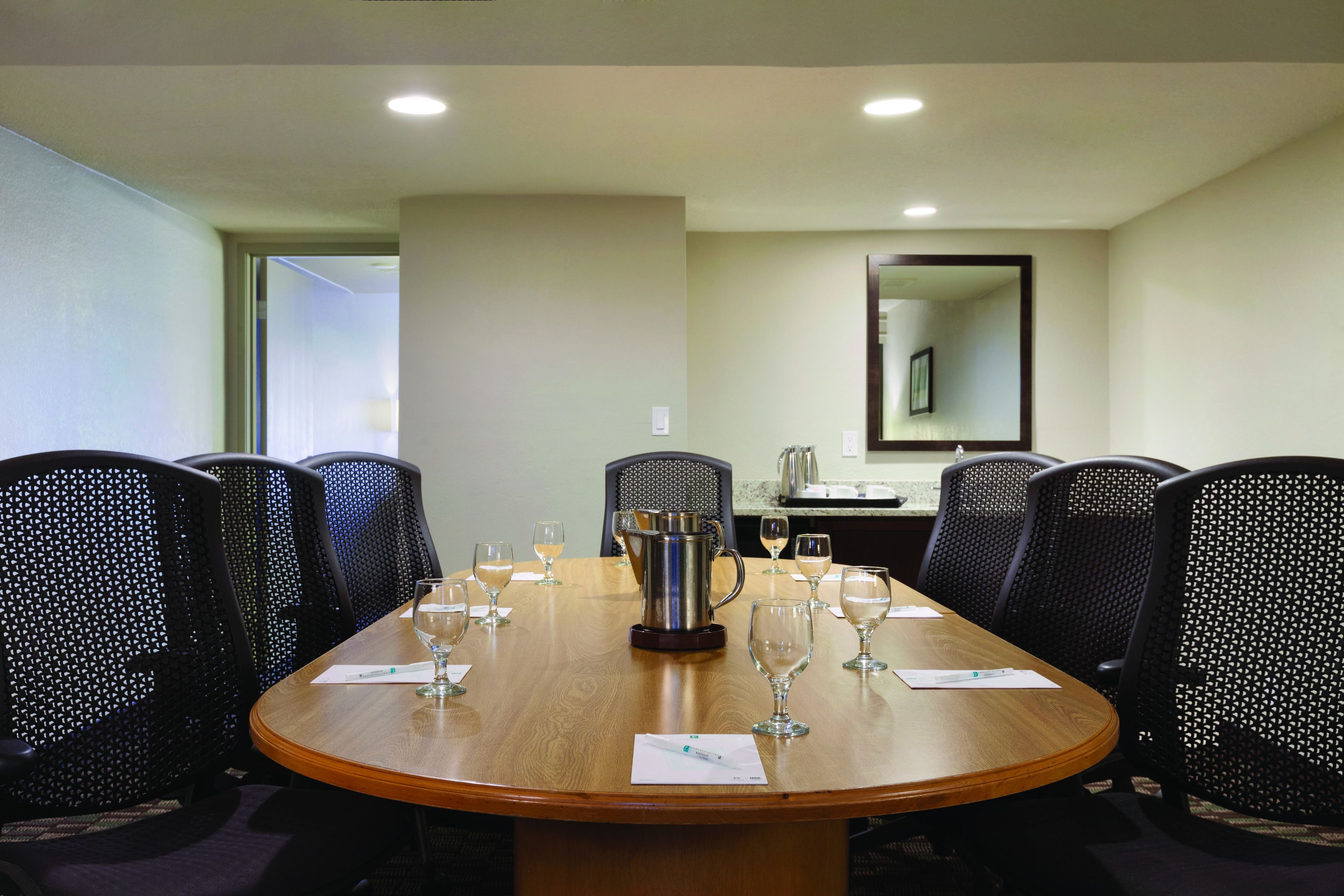 A conference room with a wooden table, black mesh chairs, and a coffee pot.