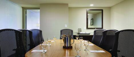 A conference room with a wooden table, black mesh chairs, and a coffee pot.