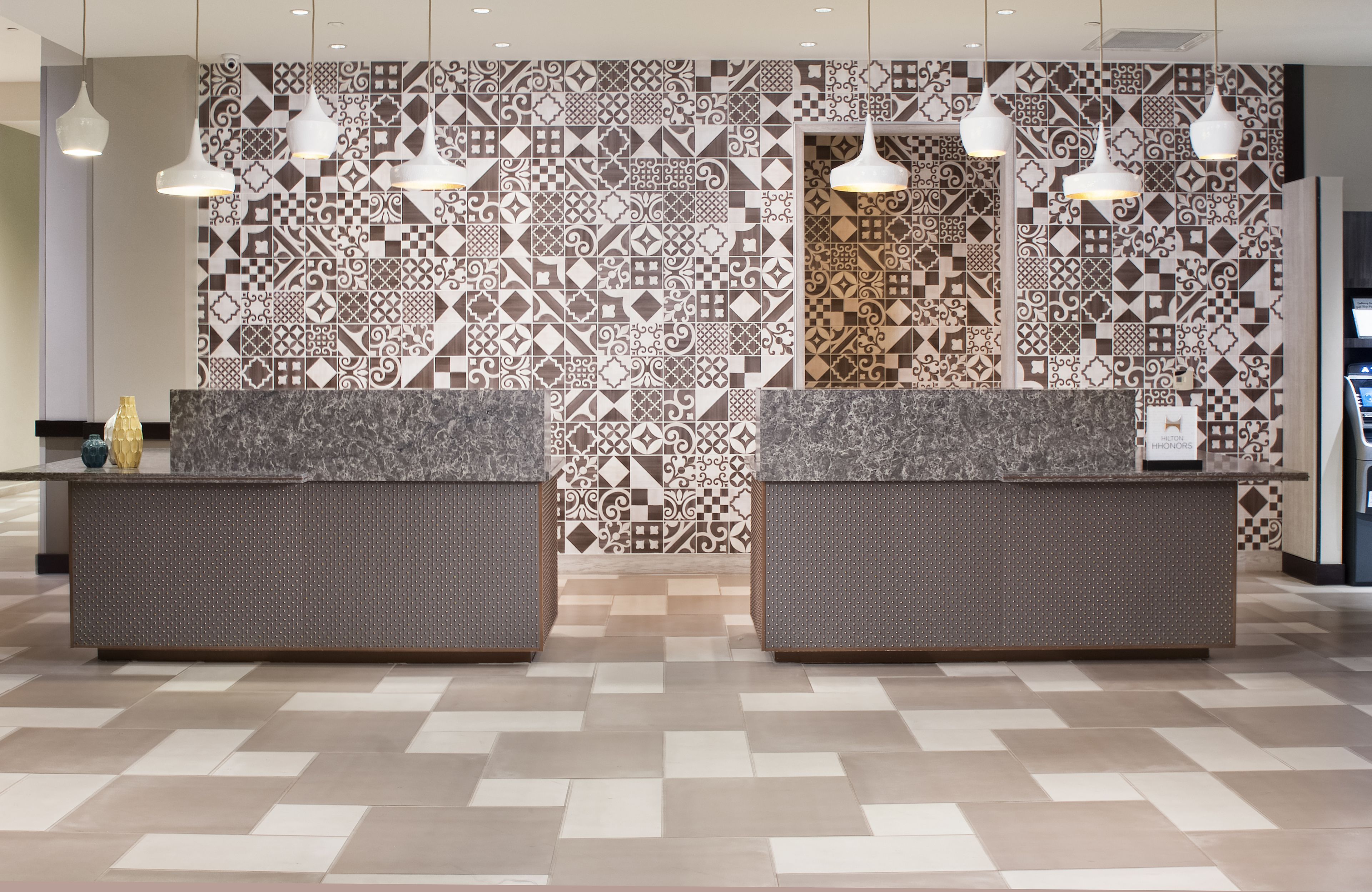 A reception area with patterned tile walls, two reception desks, and hanging pendant lights.