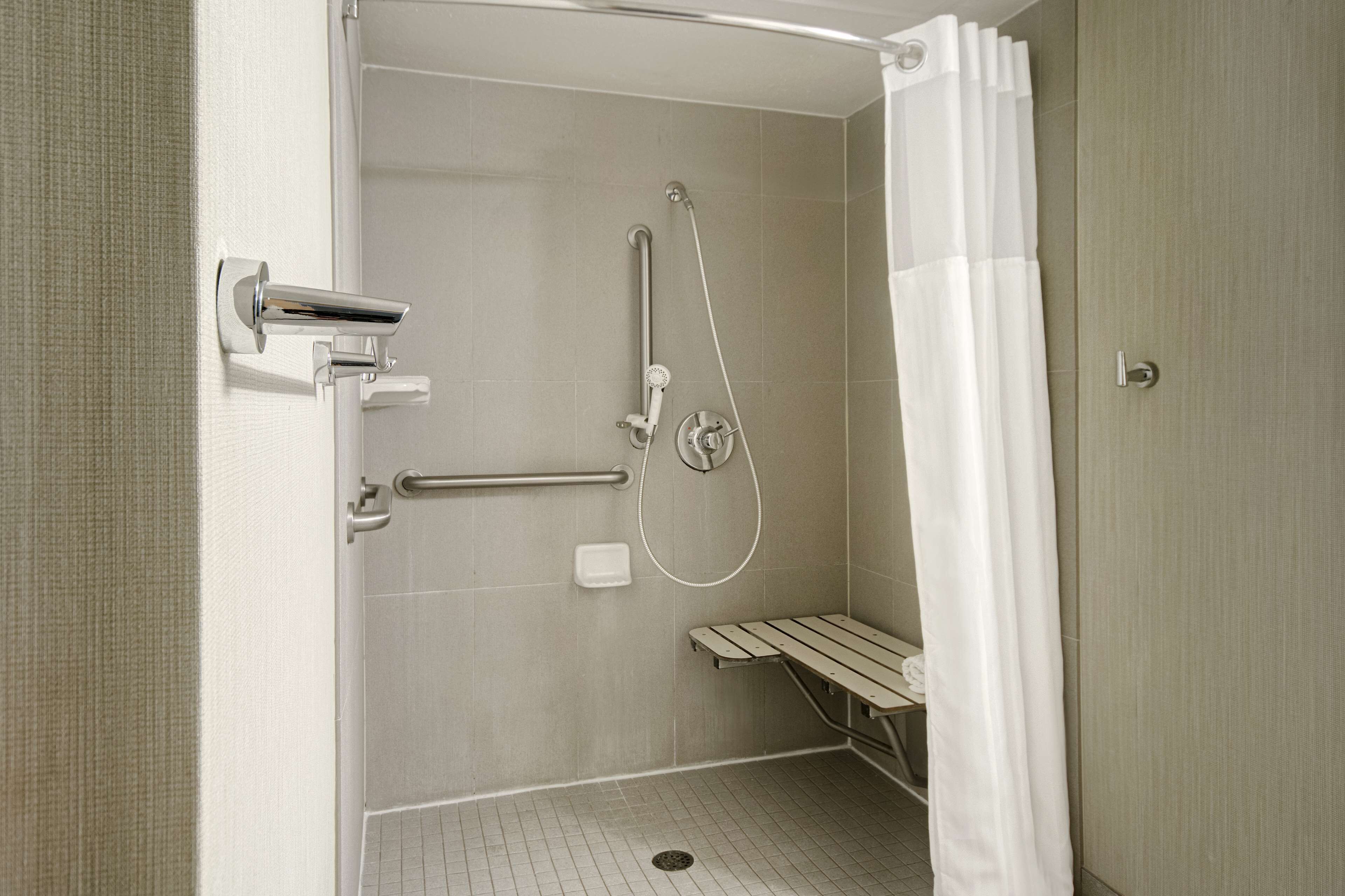 A modern shower area with a handheld showerhead, a handheld shower attachment, and a white shower curtain.