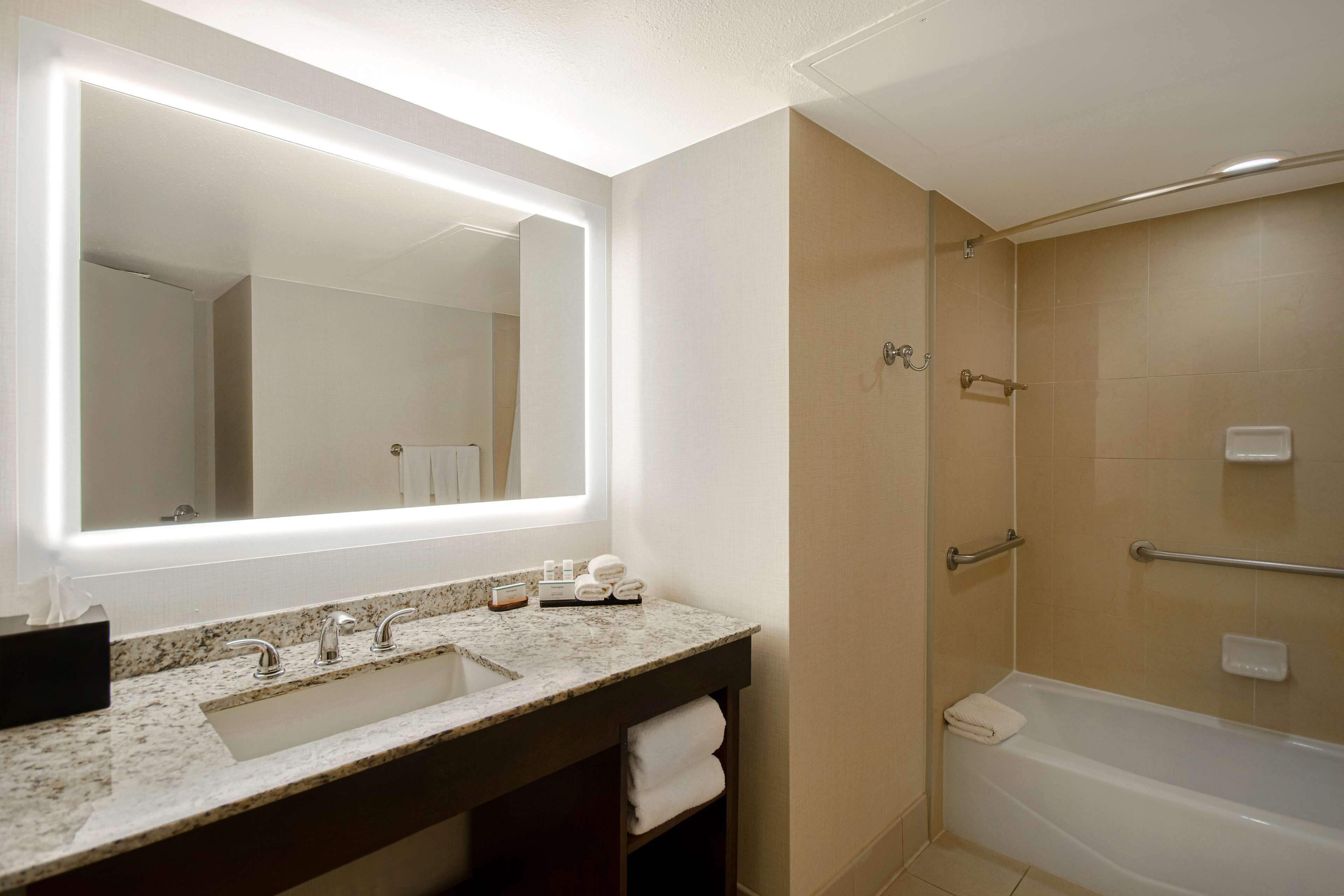 A bathroom with a large mirror, a sink with two faucets, a bathtub, and a shower area.