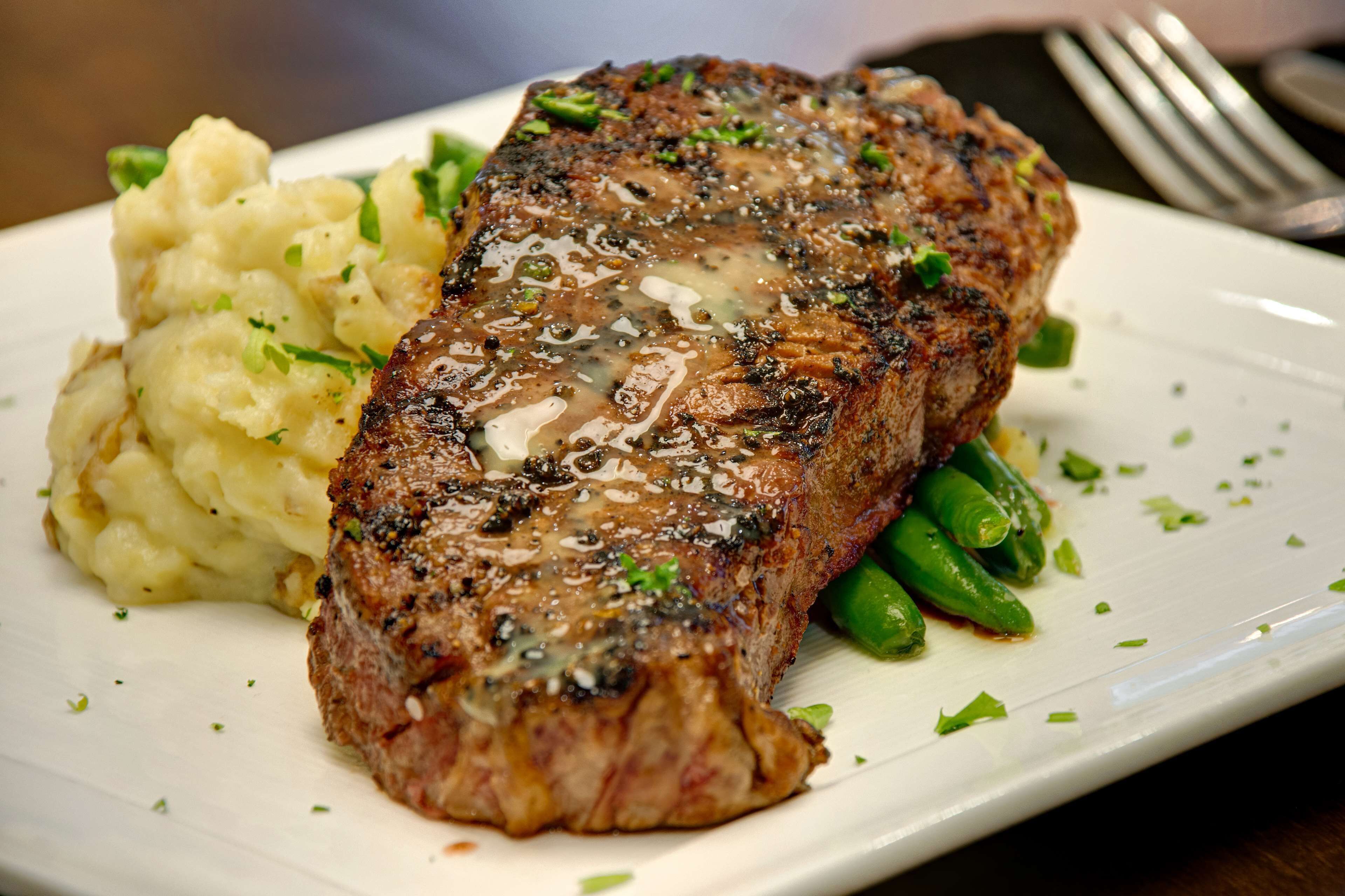 Un plato con bistec, puré de papas y judías verdes.