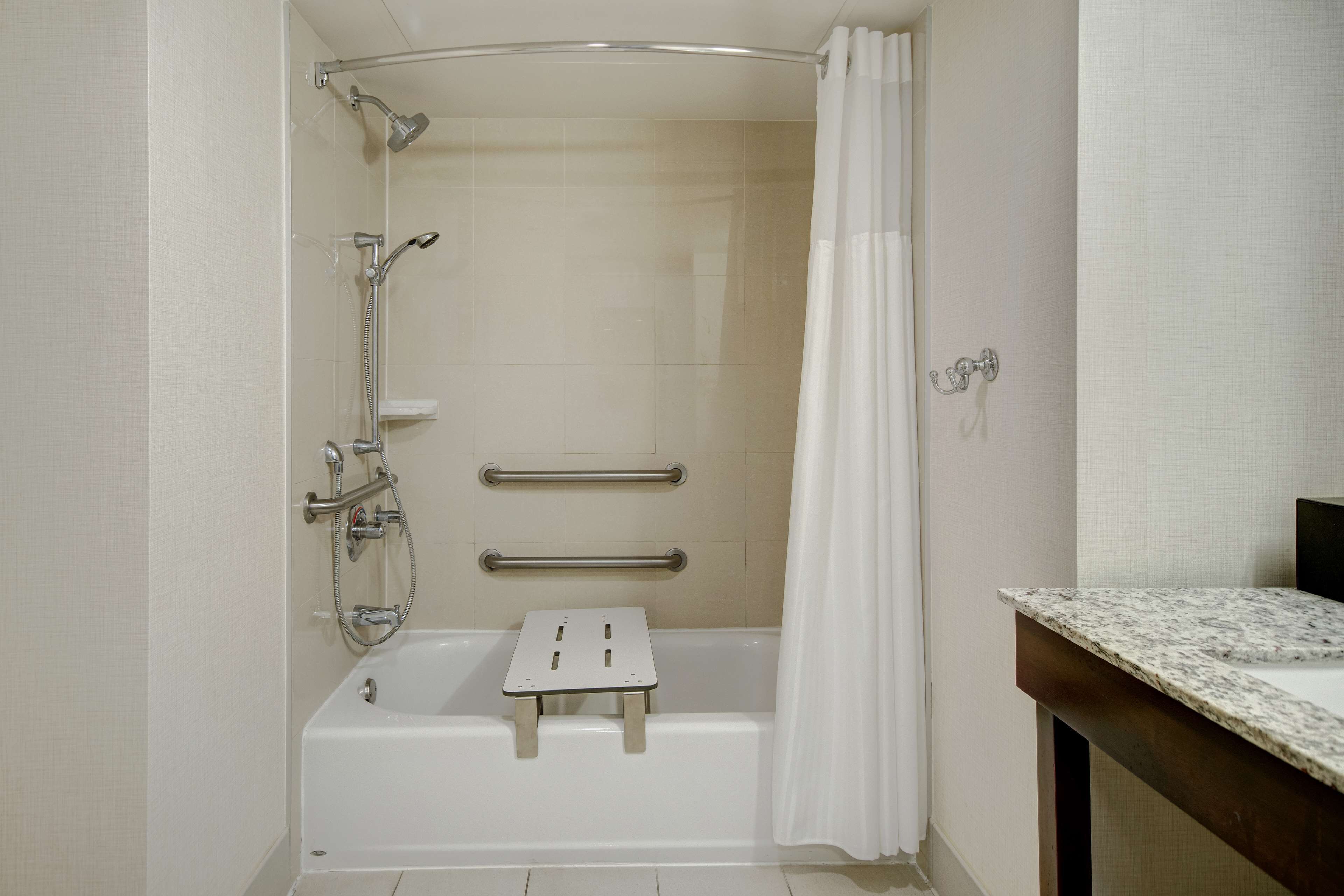 Un baño moderno con ducha a nivel de suelo, barras de apoyo y encimera de mármol.